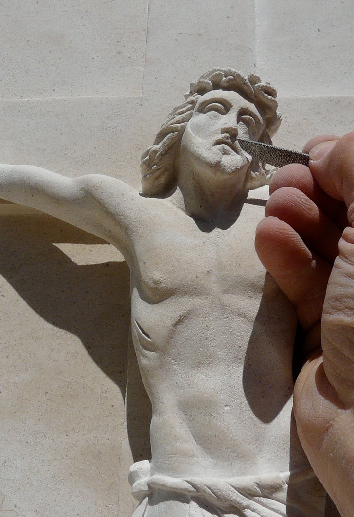Main de Jean Fournols travaillant le visage d’un crucifix en pierre